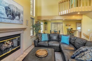 A living room with a fireplace, a black leather sofa, and a dining area in the background. - Town Shuttle|Close to Lift|BBQ|Fireplace|Garage (Breckenridge)