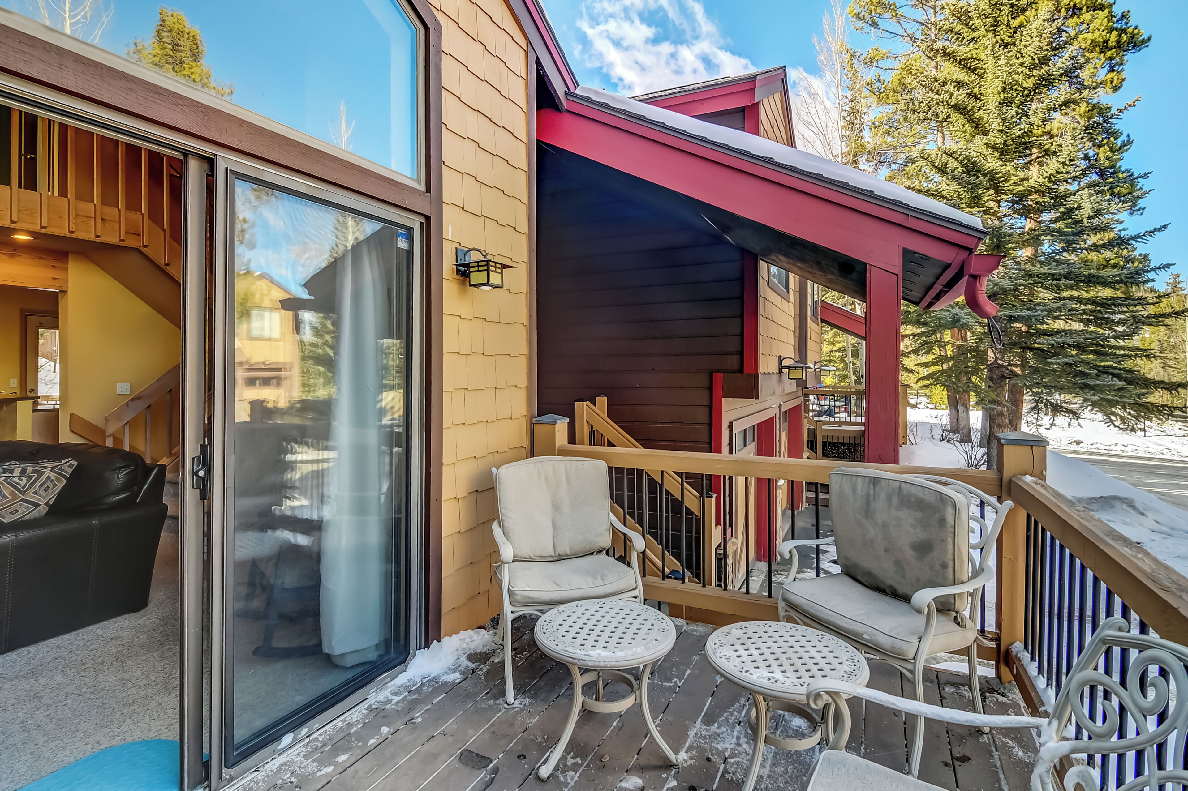A wooden exterior with a glass door, a covered outdoor seating area with two chairs and a table, and a wooden staircase leading to an upper level.