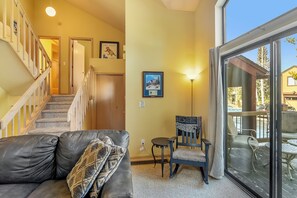 A living room with a leather couch, a small table, a chair, a staircase, and a large window with a view of the outside. - Town Shuttle|Close to Lift|BBQ|Fireplace|Garage (Breckenridge)
