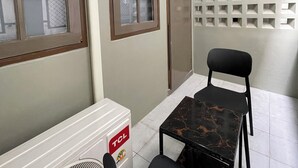 A room with a radiator, a fan, a table, a chair, and a wall with a grid pattern. - ON'S Place (Pattaya)