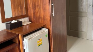 A room with a wooden wardrobe, a small white refrigerator, a mirror, and a door. - ON'S Place (Pattaya)