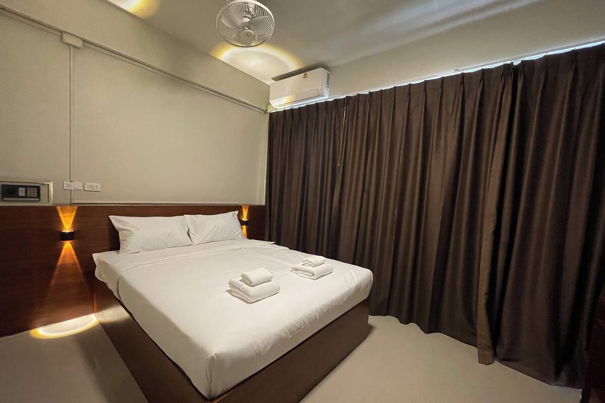 Habitación de hotel con una cama grande, ventilador de techo, aire acondicionado y ventana con cortinas.