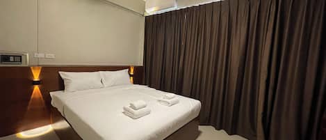A hotel room with a large bed, a ceiling fan, an air conditioning unit, and a window with curtains.