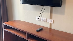 A flat-screen TV mounted on a wall above a wooden entertainment unit with a remote control on it. - ON'S Place (Pattaya)