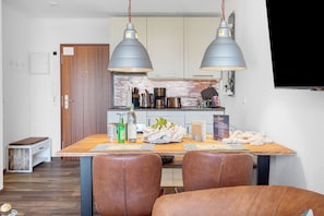 Un comedor con una mesa de madera, dos sillas de cuero marrón y dos lámparas colgantes.