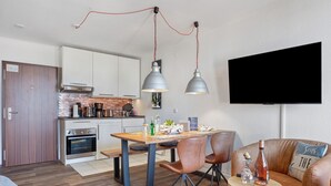 A modern kitchen with white cabinets, a dining table with chairs, a TV mounted on the wall, and a leather sofa in the living area. - Apartment in the 'Krabbenkiste' Hotel with Sea View, Shared Garden, and Wi-Fi (Wunstorf)