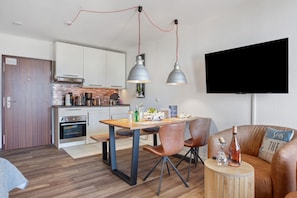 Una cocina moderna con armarios blancos, una mesa de comedor con sillas, un televisor montado en la pared y un sofá de cuero en la sala.
