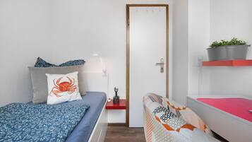 Une chambre à coucher avec un lit, une table de chevet, une étagère rouge ornée d’une plante et une porte.