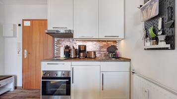 A compact kitchen with white cabinets, a stainless steel oven, a coffee maker, and a pegboard with kitchen utensils.