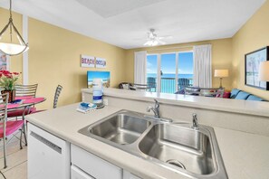 A kitchen with a double sink, a dining area with chairs and a table, and a view of the ocean through a window. - 🌊Stunning Gulf Views | 2 Pools | Great Location | Seychelles 603🌊 (Panama City Beach)