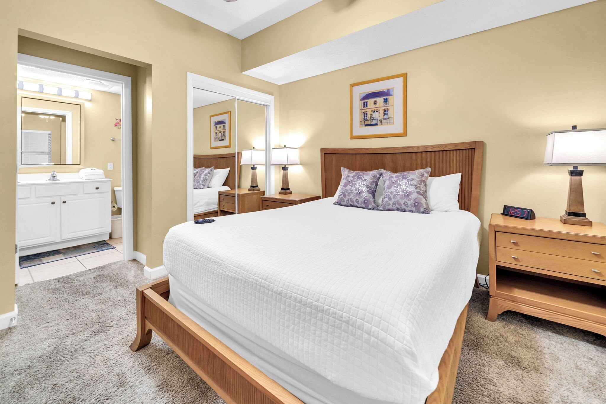 A hotel room with a large bed, a bedside table with a lamp, a nightstand, a mirror, and a framed picture on the wall.