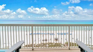 Blick auf einen Strand vom Balkon mit Geländer, Strandstühlen und Sonnenschirmen.