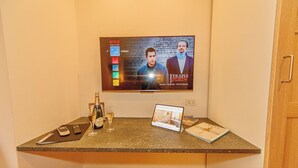 Huoneessa on televisio, jossa näkyy elokuvan juliste, pieni pöytä, jossa on kannettava tietokone, pullo viiniä ja lasi.