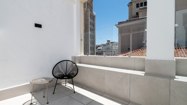 A balcony with a chair, a small table, and a view of buildings. - 504 - A33 Signature | Penthouse | Terr | 2BR | 6G (Madrid)