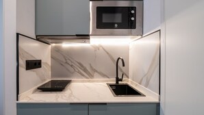 A compact kitchen with a built-in microwave, a sink, and a sleek countertop. - 504 - A33 Signature | Penthouse | Terr | 2BR | 6G (Madrid)