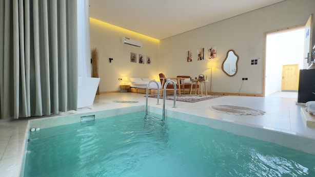 A modern hotel room with a swimming pool, a sofa, a dining table, and a mirror.