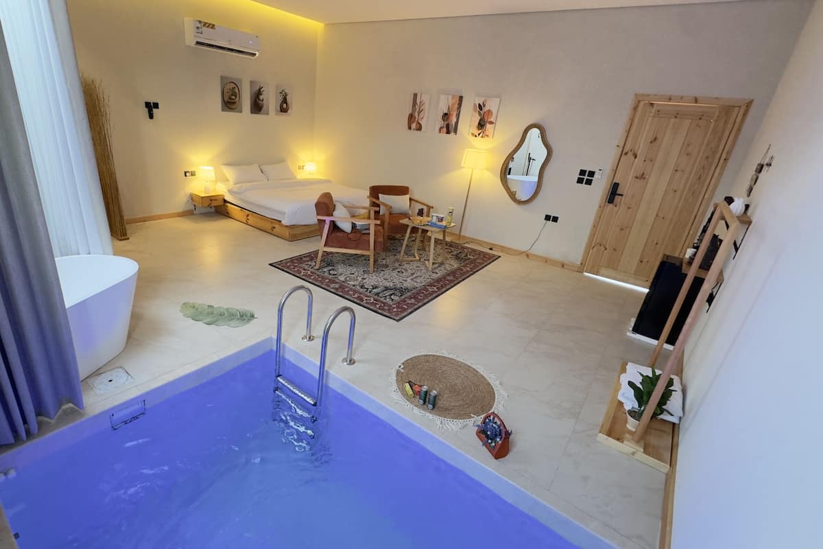 A modern hotel room with a large bathtub, a bed, a sofa, and a small table.