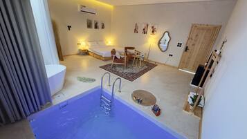Una habitación de hotel moderna con una bañera grande, una cama, un sofá y una mesita.