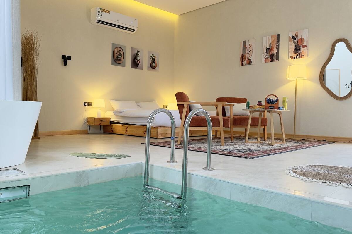 A modern hotel room with a pool, a bed, a desk, and a chair.