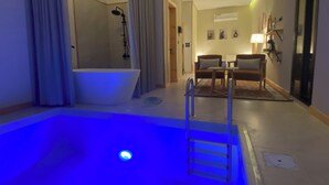 A hotel room with a bathtub, a small table with chairs, a lamp, and a wall-mounted air conditioner.