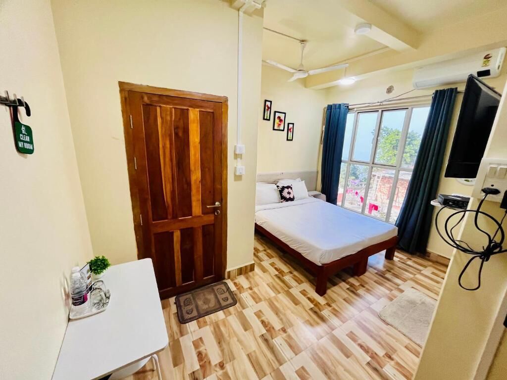 A bedroom with a bed, a desk, a TV, and a window with curtains.