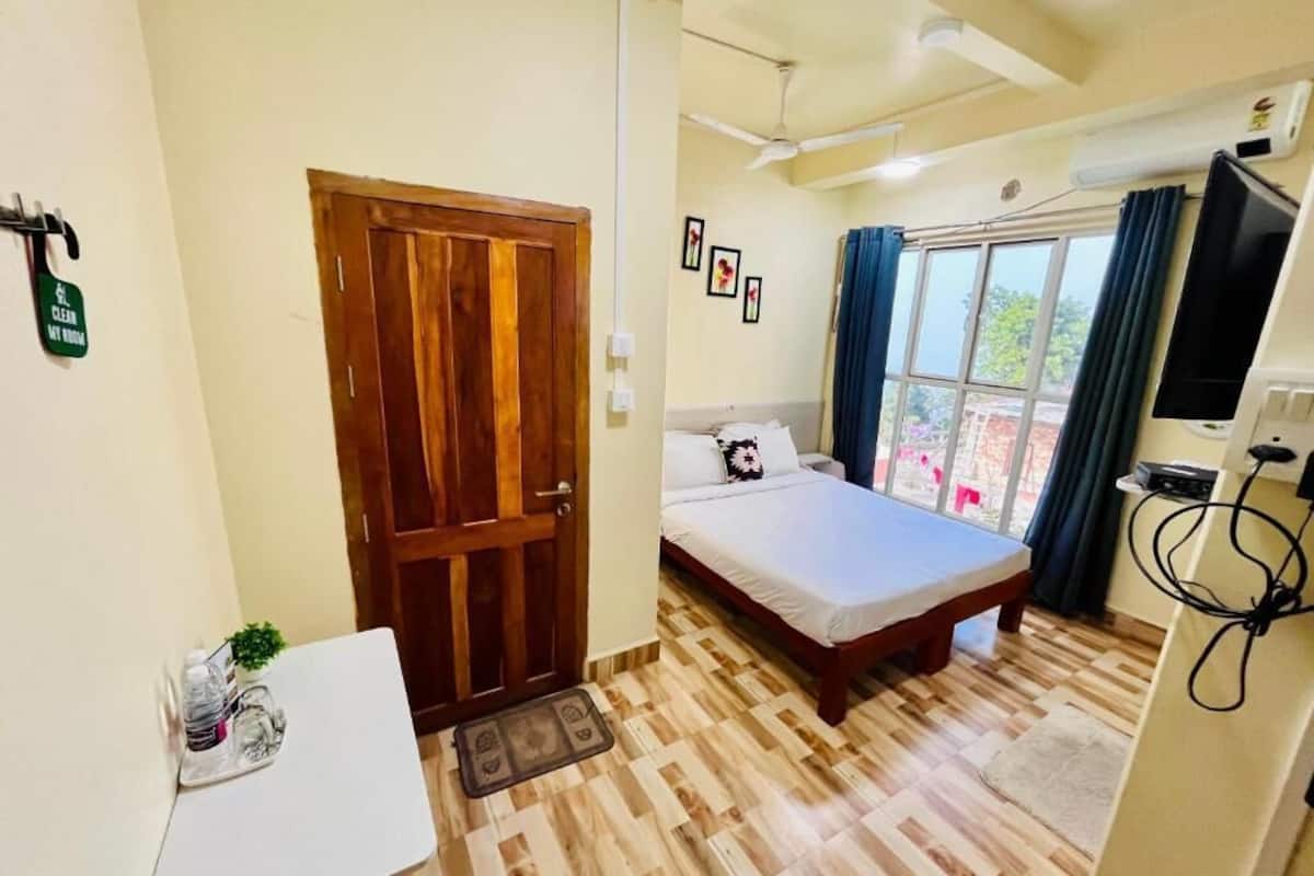 A bedroom with a bed, a desk, a TV, and a window with curtains.
