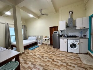 A compact hotel room with a bed, a small kitchenette, a washing machine, and a ceiling fan. - Aizawl Guest House (Aizawl)