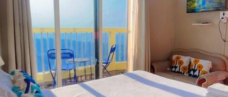 A hotel room with a large bed, a balcony with chairs, and a TV on the wall.