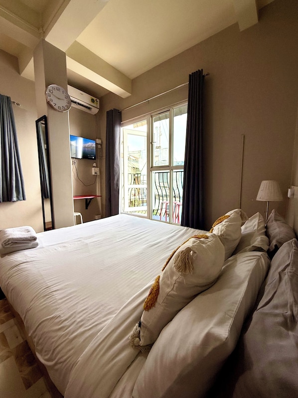 Una habitación de hotel con una cama grande, un televisor, un balcón con vistas y aire acondicionado.