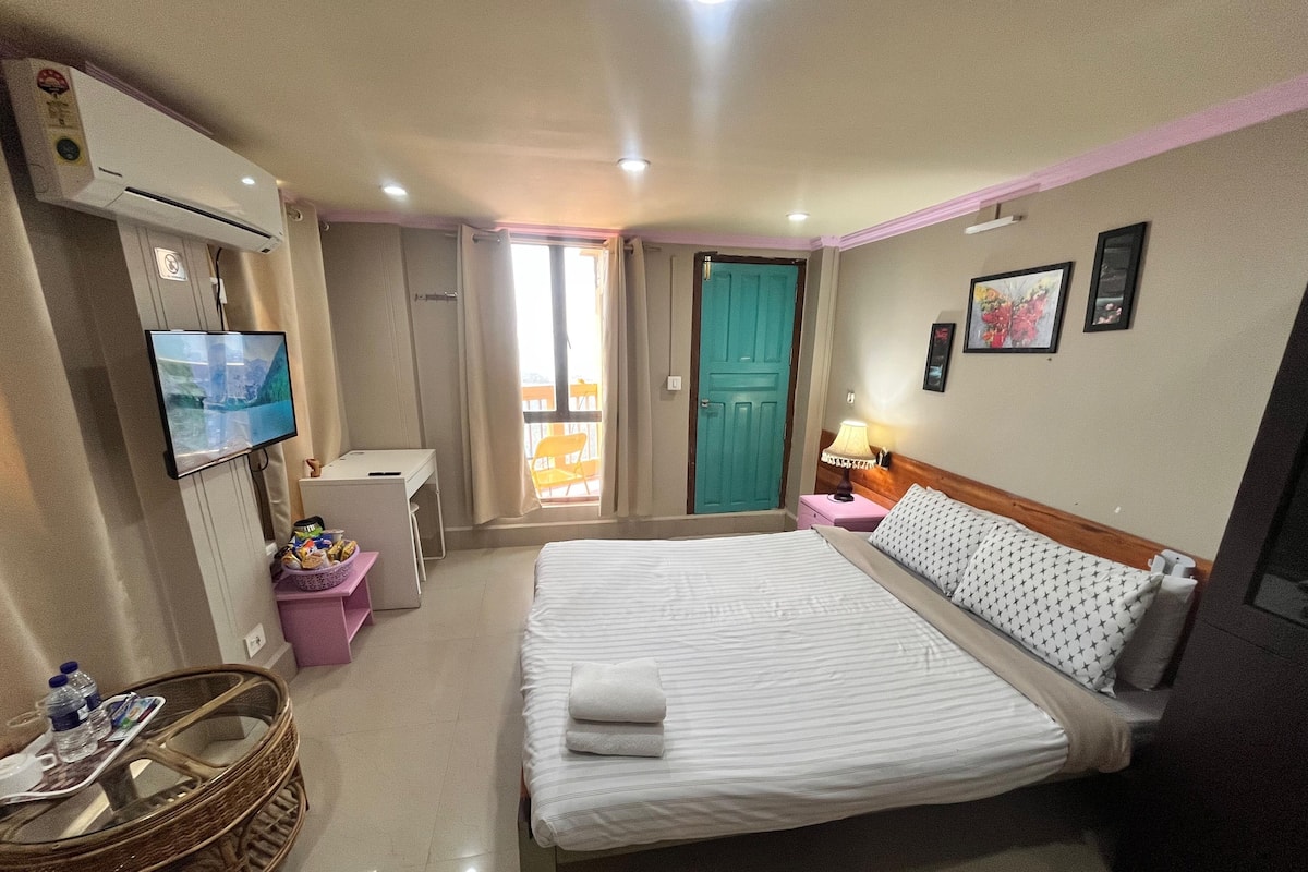 Une chambre d’hôtel avec un lit, un bureau, une télévision, une fenêtre avec des rideaux et une porte.