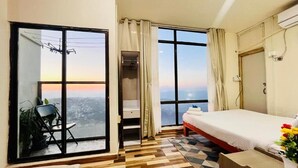 Ein Hotelzimmer mit großem Fenster, einem Bett, einem Schreibtisch und einem Stuhl.