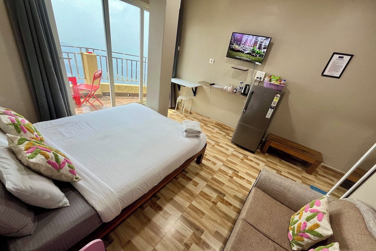 Une chambre d’hôtel équipée d’un lit, d’un canapé, d’une télévision, d’un réfrigérateur et d’un balcon avec vue.