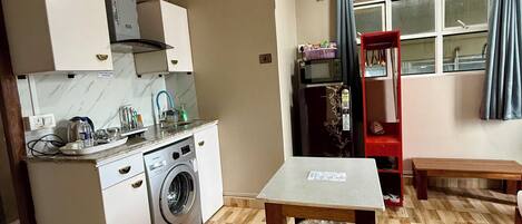 Una cocina compacta con lavadora, microondas y un pequeño comedor con mesa y banco.