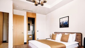 Een moderne hotelkamer met een groot bed, een houten garderobe, een badkamer met een glazen deur en een plafondlamp.