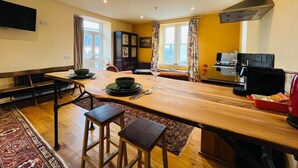 Een keuken met een houten tafel, barstoelen, een koffieapparaat en een aan de muur bevestigde televisie.