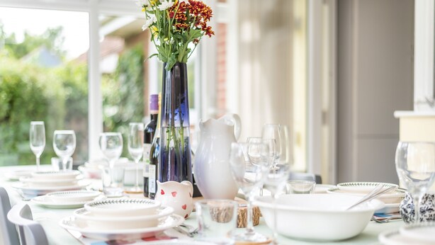 A dining table set with plates, glasses, and a pitcher, with a vase of flowers in the center. - Harpers - sleeps 6 guests  in 3 bedrooms (Burnham Market)