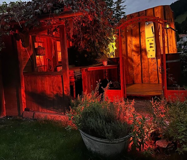 A rustic wooden structure with a small porch and a door, surrounded by greenery.