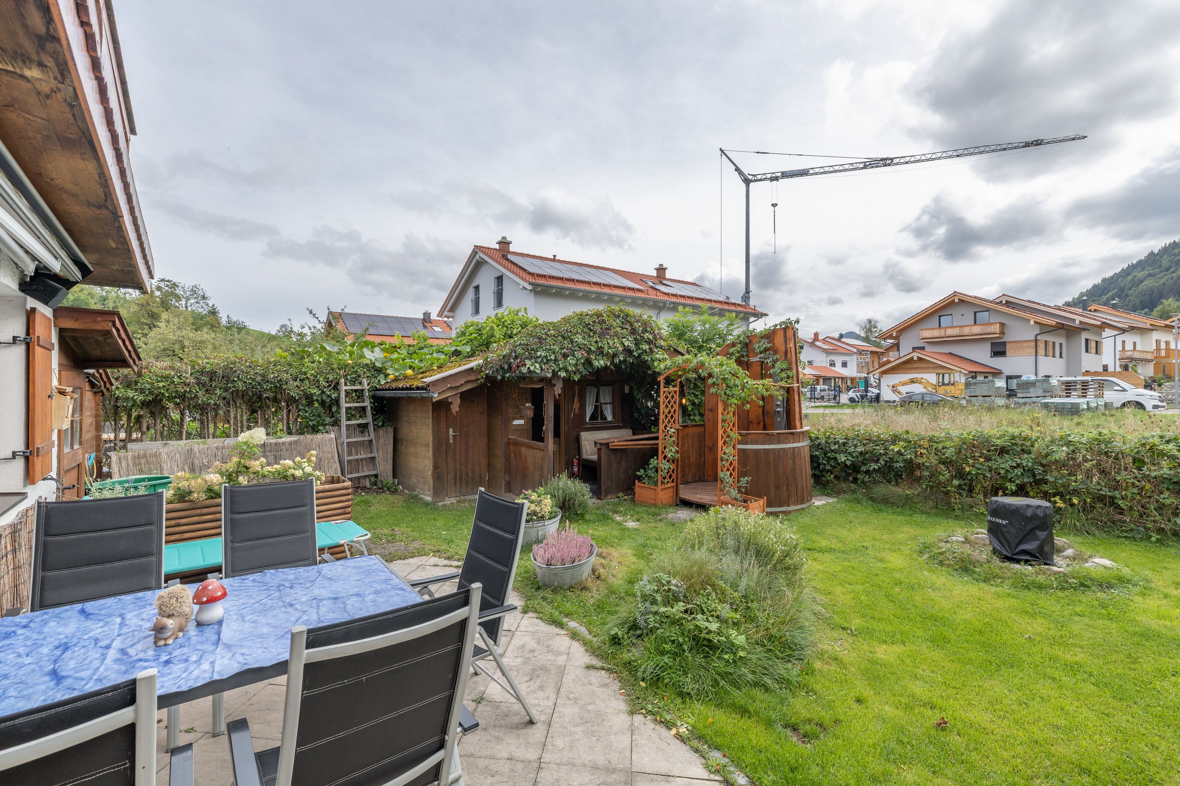Ein Wohngebiet mit einer Terrassentischgruppe, einer hölzernen Pergola und Blick auf die Nachbarhäuser.