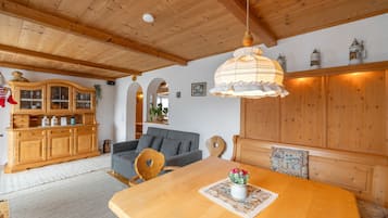 Una habitació acollidora amb bigues de fusta, una taula de dinar amb un ram de flors, un sofà i un armari amb portes de vidre.