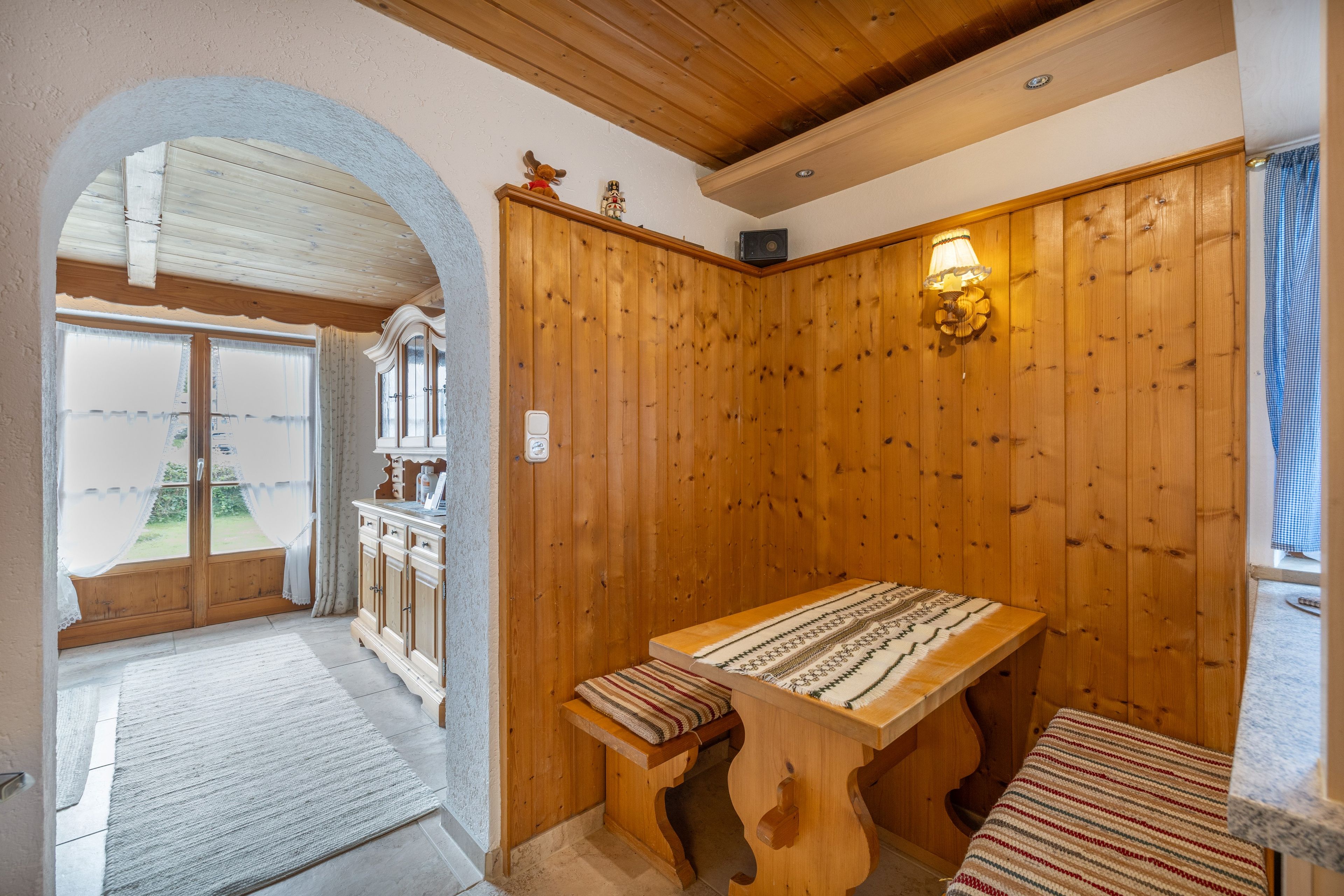 A room with a wooden table, a bench, and a view through an arched doorway.