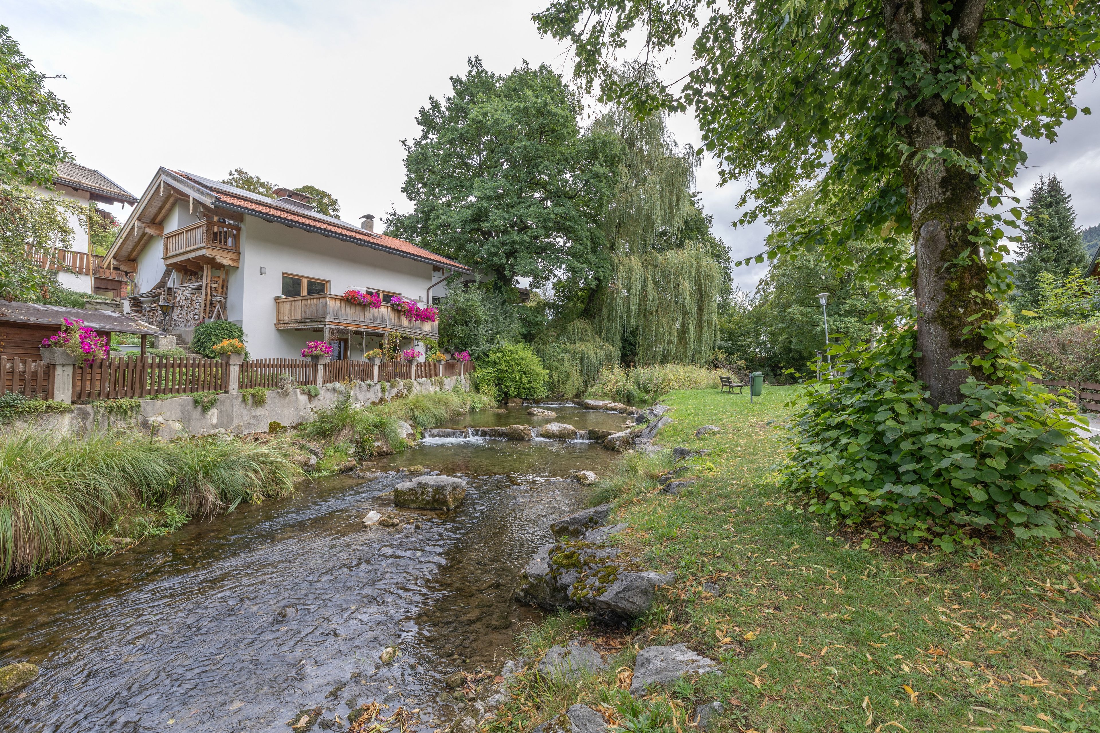 Ein traditionelles Chalet mit Holzbalkon, einem kleinen Bach und üppigem Grün.
