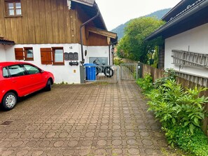A paved driveway leading to a wooden house with a red car parked on the left.