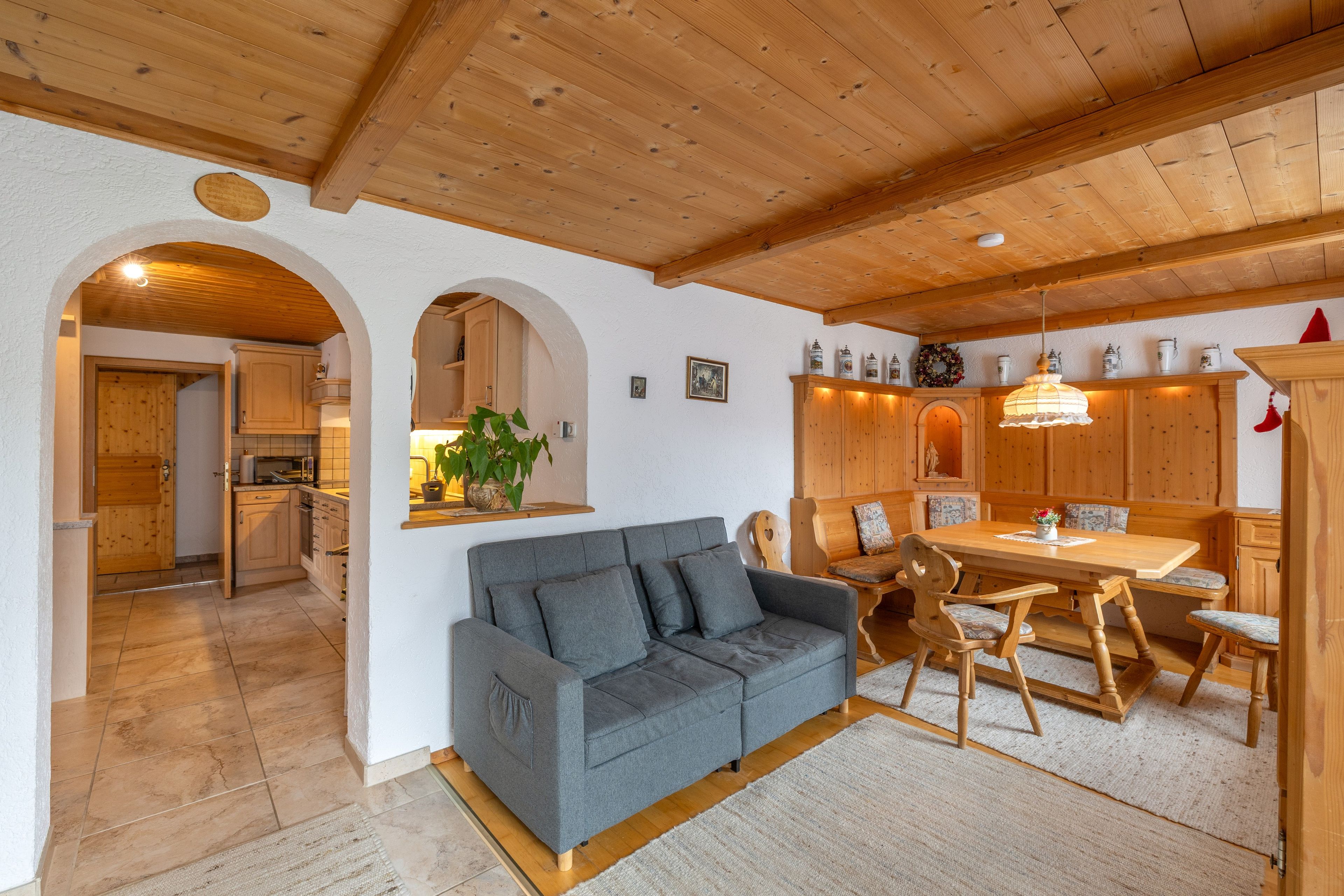 Ein gemütliches Wohnzimmer mit grauem Sofa, einem Holzespeisetisch und einer Küche im Hintergrund.