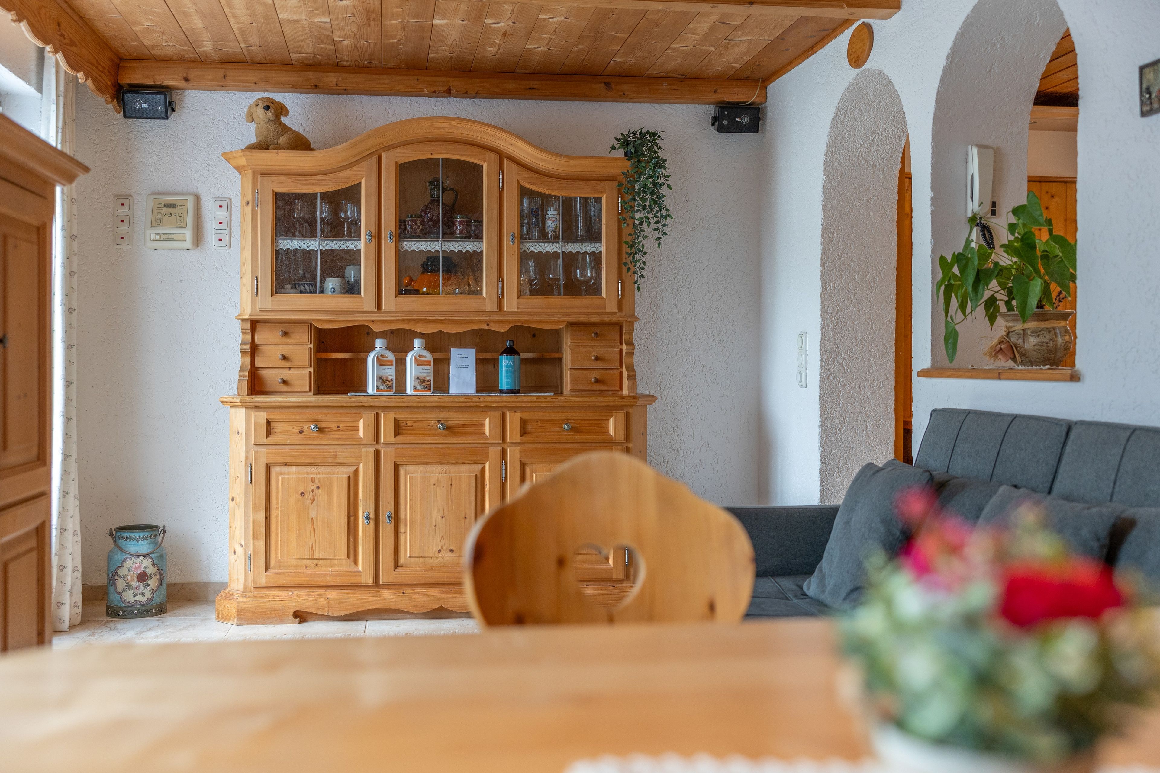 Ein Holzkabinett mit Glastüren, ein Esstisch mit Stuhl und ein Sofa in einem Raum mit Holzboden und weißen Wänden.