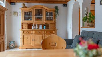 Ein Holzkabinett mit Glastüren, ein Esstisch mit Stuhl und ein Sofa in einem Raum mit Holzboden und weißen Wänden.