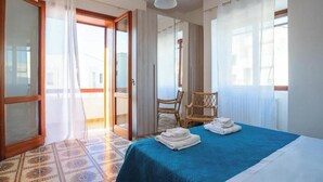 Una camera d'albergo con un letto, una sedia, una finestra con tende e una porta che dà su uno spazio all'aperto.