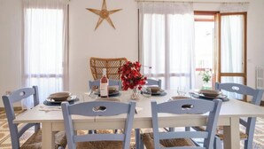 Zona pranzo con tavolo apparecchiato per quattro, sedie bianche, decorazione a stella sul muro e una finestra con tende.