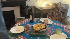 Uma mesa de jantar posta, com pratos, uma tigela de massa, uma garrafa de vinho e um copo.