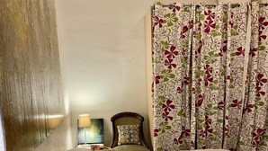Quarto com cama, cadeira, abajur e cortina estampada com flores.