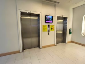 Un ascensor con pantalla digital, instrucciones de emergencia y extintor.